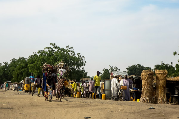 Women carrying wood, woven thatch mats for sale by the roadside in Monguno, Borno State, Nigeria